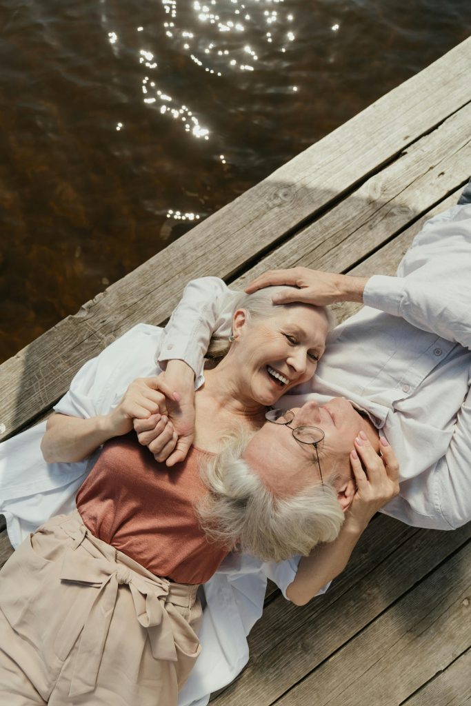 A joyful senior couple lying on a dock by the lake, embracing with love and laughter.